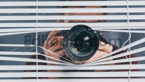 close-up view of young man holding camera and taking pictures through blinds