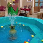 Fountain of a blue color pool splashes water drops on surface citrus orange apple flowers float on t