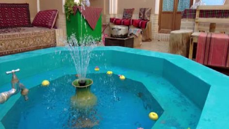 Fountain of a blue color pool splashes water drops on surface citrus orange apple flowers float on t